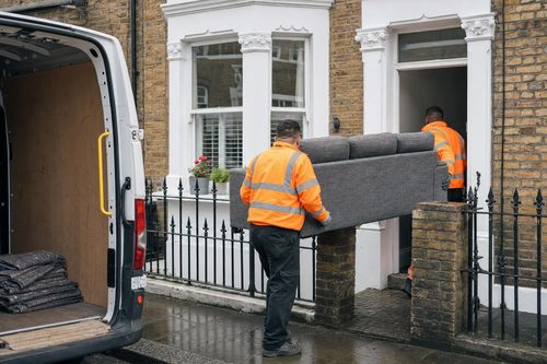 Two movers carrying a sofa out of a Victorian terraced house in London