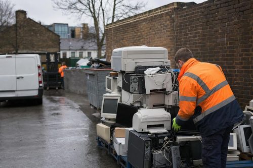 Crew member stacking old printers and computers for WEEE recycling in London