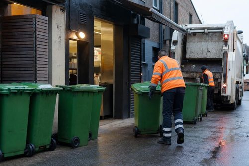 Green food-waste bins at a London restaurant back door at dawn, being wheeled to a collection lorry