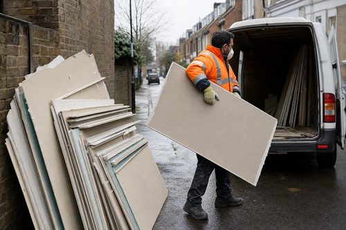 Crew member carrying plasterboard sheets to a van on a London street