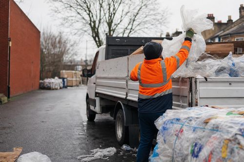 Crew member loading baled plastic waste onto a tipper van in a London street