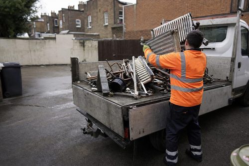 Crew member loading scrap metal onto a tipper van in a London yard