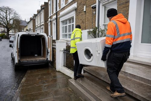 Workers carrying a washing machine out of a London flat to a van
